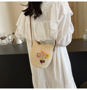 Detail of hand-woven straw crossbody bucket bag featuring colorful floral embellishments