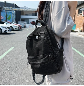 Detail of black washed denim backpack featuring vintage texture and silver metal zippers