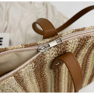 Detail of woven straw tote bag featuring brown leather handle and silver zipper closure