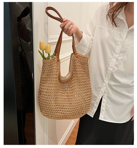 Detail of woven straw tote bag with brown leather handle and rivet accents