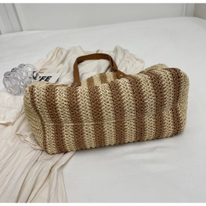 Macro detail of large straw tote bag with brown leather handles and striped weaving