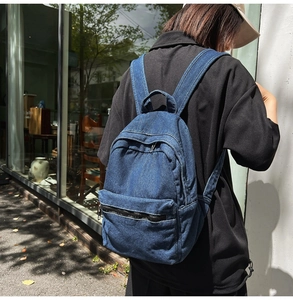 Side view of blue washed denim backpack with wide straps on a model in urban street setting