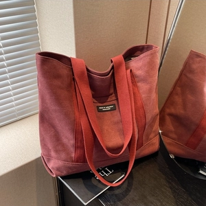 Minimalist burgundy canvas tote bag with wide straps and black label in a cozy indoor setting