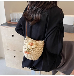 Detailed view of woven straw bucket bag with floral accent and brown shoulder strap