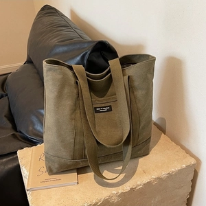 Olive green canvas tote bag with black logo patch on a textured stone surface