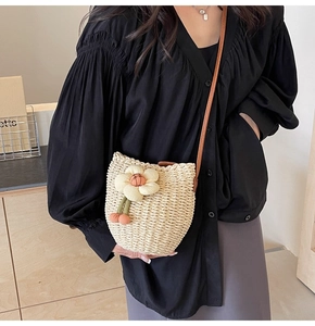 Detail of cream woven straw bucket bag with floral decor and brown leather strap