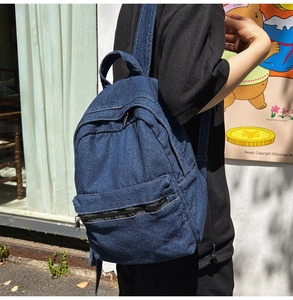 Deep blue denim backpack with front zipper pocket shown in a casual urban street setting