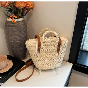 Straw handbag with brown leather straps and drawstring pouch on a white table