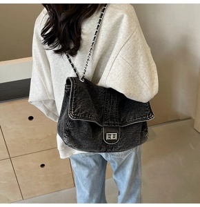Detailed view of black denim crossbody bag featuring metal chain strap and turn-lock