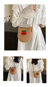 Detail of woven straw bucket bag with red cherry ornaments and brown leather strap