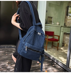 Side view of a dark blue denim backpack worn by a model in a casual lifestyle setting