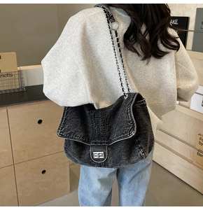 Detail of washed black denim crossbody bag with silver chain strap and metal turn-lock