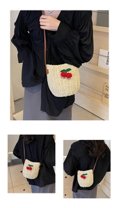 Detail of beige woven bucket bag featuring 3D red cherry accents and leather strap