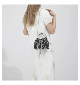 Detail of black fabric crossbody bucket bag with floral embroidery and tassel on model
