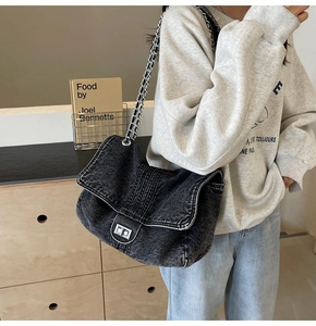 Detail of black denim crossbody bag featuring a silver metal chain strap and twist lock
