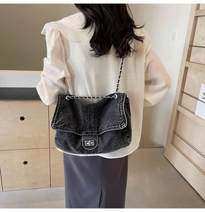Detail of black denim crossbody bag featuring metallic chain strap and twist lock