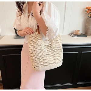 Detail of handwoven straw tote bag with brown leather shoulder strap shown on model