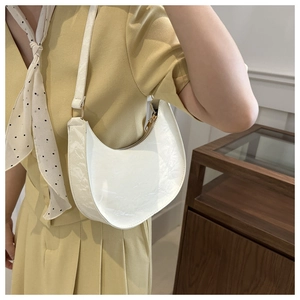 Detail view of a white crescent shoulder bag in glossy patent PU leather on a model