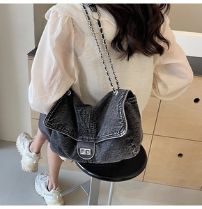 Detailed close-up of dark denim shoulder bag with silver chain strap and twist lock