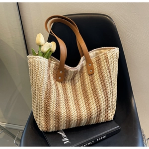 Detail of hand-woven straw tote bag texture and brown faux leather handle with rivets