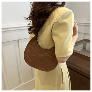 Detail view of brown pleated PU leather crescent bag shown on model in minimal setting