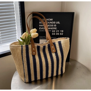 Detail of blue and white striped straw tote bag featuring leather handles and zipper