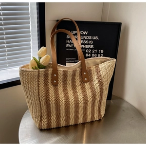 Close-up of woven straw tote bag featuring vertical stripes and brown leather handles