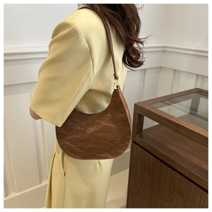 Detail of a brown crescent-shaped PU leather shoulder bag with wrinkled texture and gold buckle