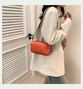 Detail der orangefarbenen Crossbody-Tasche aus PU-Leder mit Narbenprägung am Model
