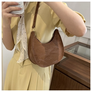Brown pleated faux leather crescent shoulder bag shown on model for size perspective