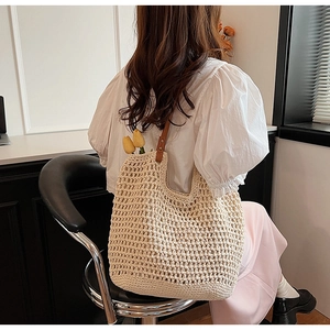 Detail view of woven straw shoulder bag with brown leather straps and rivet accents