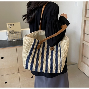Detail of a large striped straw tote bag with brown leather straps worn by a model