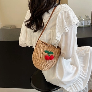 Fashionable woven straw bucket bag with red cherry accents and brown leather strap