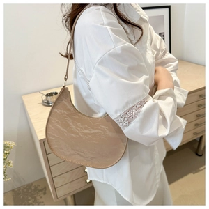 Detail of beige crescent shoulder bag showing pleated PU leather texture and slim strap