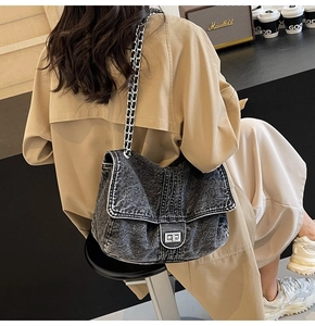 Detail of black denim crossbody bag featuring silver turn-lock and white contrast stitching