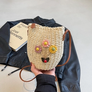 Beige woven straw bucket bag with floral accents and brown shoulder strap accessory