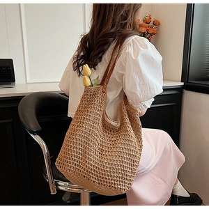 Detail of hand-woven straw tote bag with brown leather handle and reinforced rivets