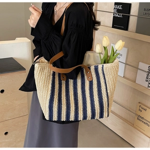 Detailed view of striped woven straw tote bag with brown leather handles and metal rivets
