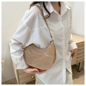 Close-up of beige moon bag with glossy pleated texture and adjustable strap detail