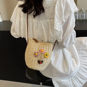 Straw woven bucket bag with 3D floral accents and brown strap shown in side view