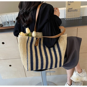 Straw tote bag with blue stripes and brown straps worn by a model in a minimal room
