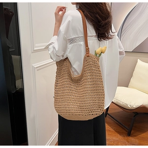 Detail of straw woven tote bag featuring brown leather shoulder straps and rivets