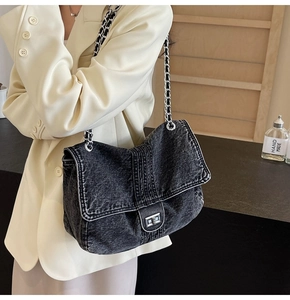 Detail of grey denim crossbody bag with silver chain strap on cream blazer