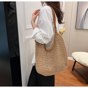 Detail of woven straw tote bag with brown faux leather straps and bronze rivet accents