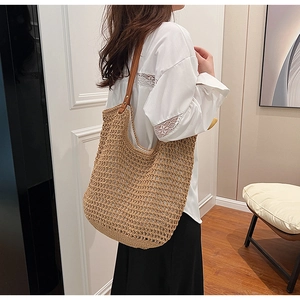 Close-up of woven straw tote bag with brown leather straps and rivet details
