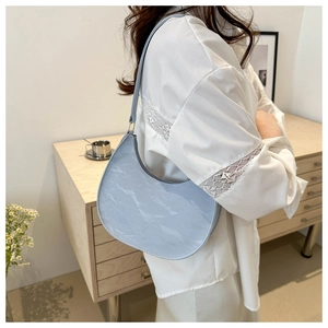 Close-up of light blue crescent PU shoulder bag with pleated texture and gold hardware