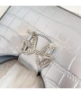 Close-up of silver PU crossbody bag with crocodile texture and rhinestone bow clasp