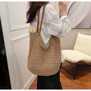 Detail of hand-woven straw shoulder bag with dark brown leather straps and metal rivets