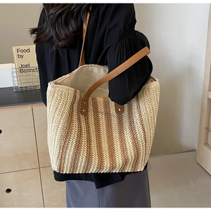 Detailed side view of large woven straw tote with leather straps on a female model