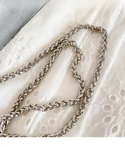 Close-up of woven silver metal chain strap for women's crossbody bags on white fabric